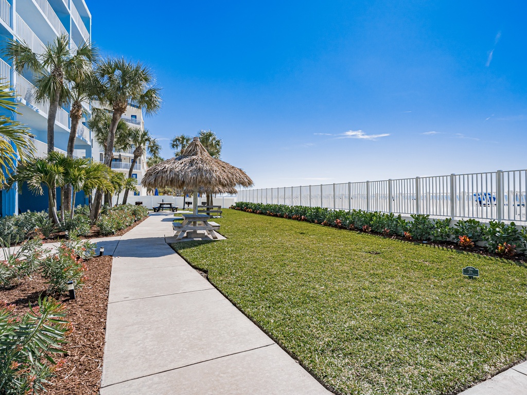 A tropical oasis featuring manicured lawns, swaying palms, and a charming thatched-roof gazebo perfect for seaside relaxation.