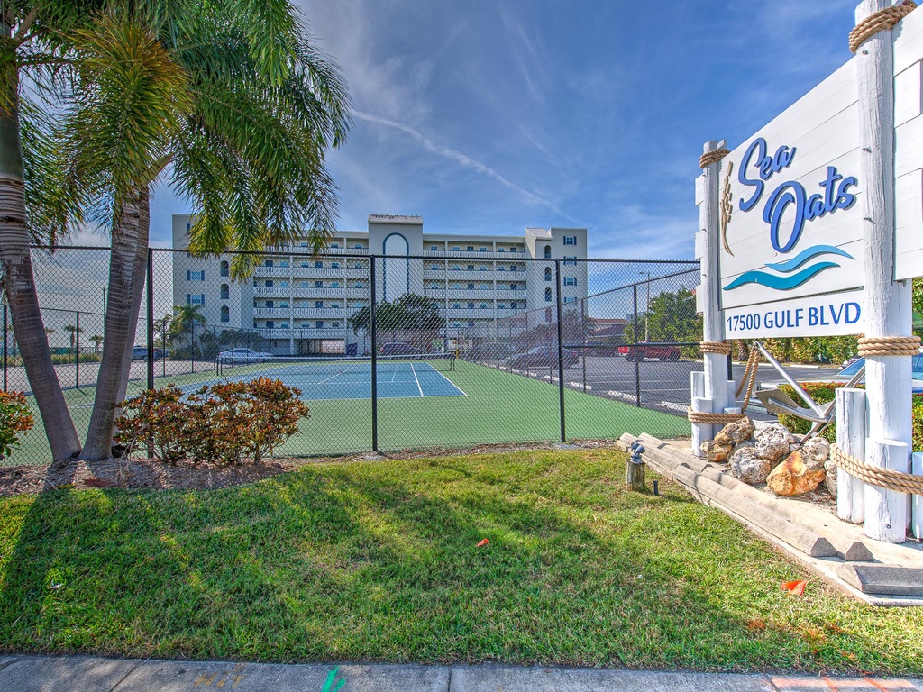 Sea Oats resort entrance welcomes guests to coastal comfort with tennis courts and tropical landscaping along Gulf Boulevard.