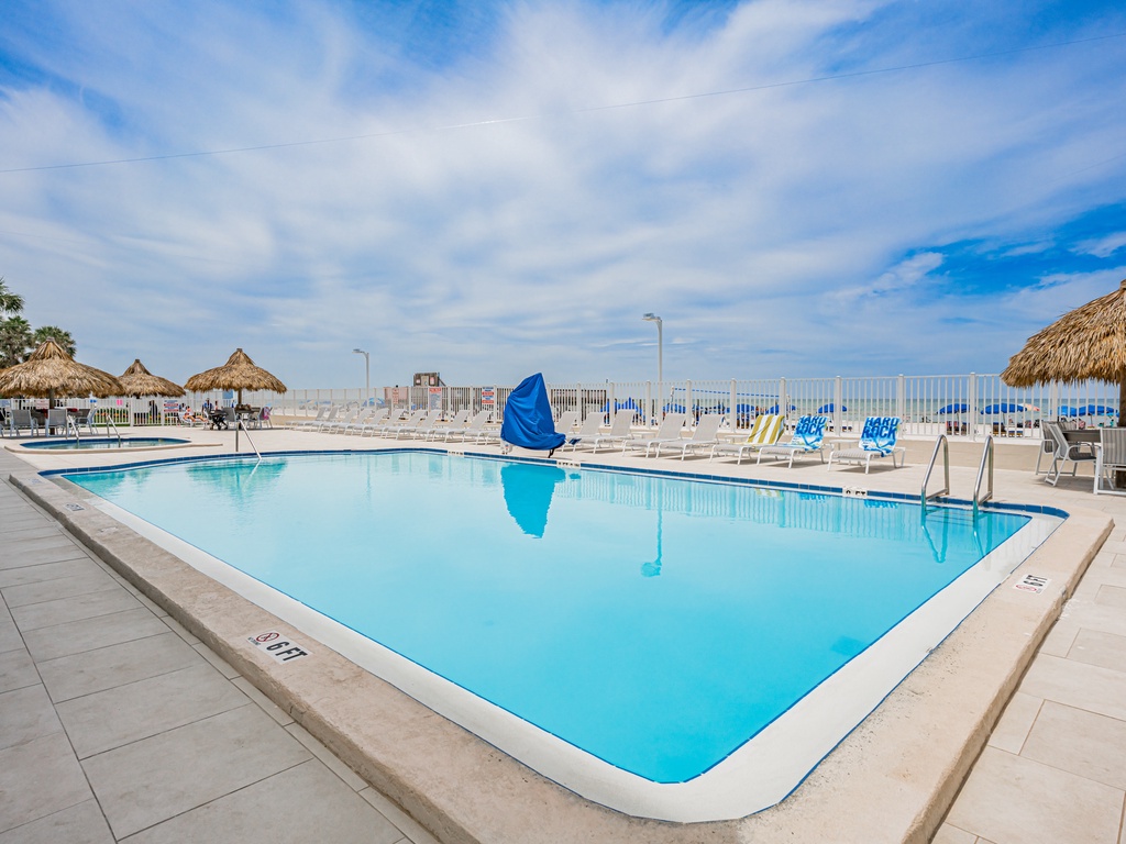 Crystal-clear pool with thatched umbrellas and lounge chairs creates your perfect sunny retreat.