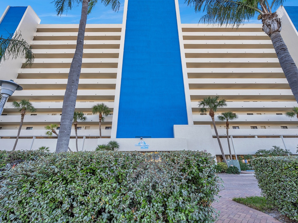 Modern beachfront hotel with distinctive blue and white architecture surrounded by swaying palm trees.