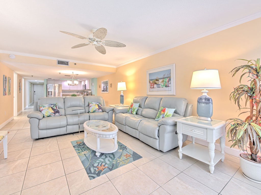 Sink into plush gray sofas in your bright, coastal-inspired living room where tropical touches and warm lighting create the perfect retreat.