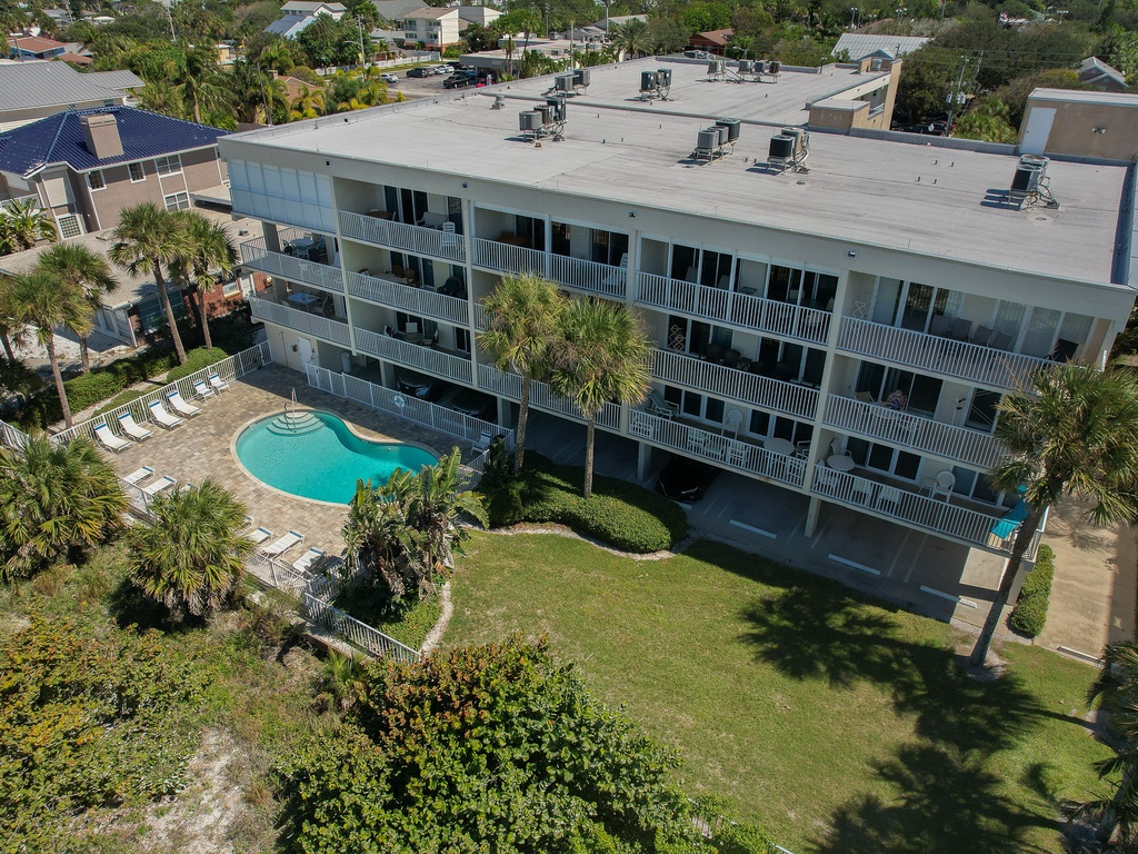 Aerial view of a three-story vacation rental property featuring a sparkling pool surrounded by tropical landscaping and palm trees.