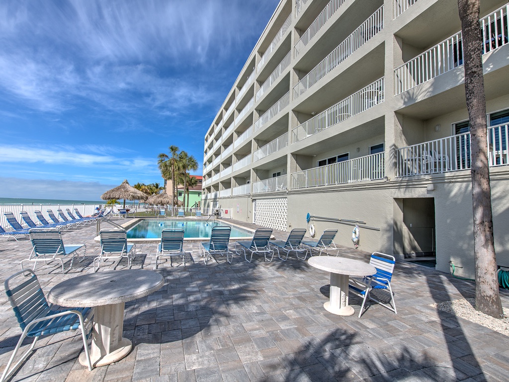 Multi-story beachfront property featuring an outdoor pool deck with lounge chairs and dining tables, steps from the sandy shore.