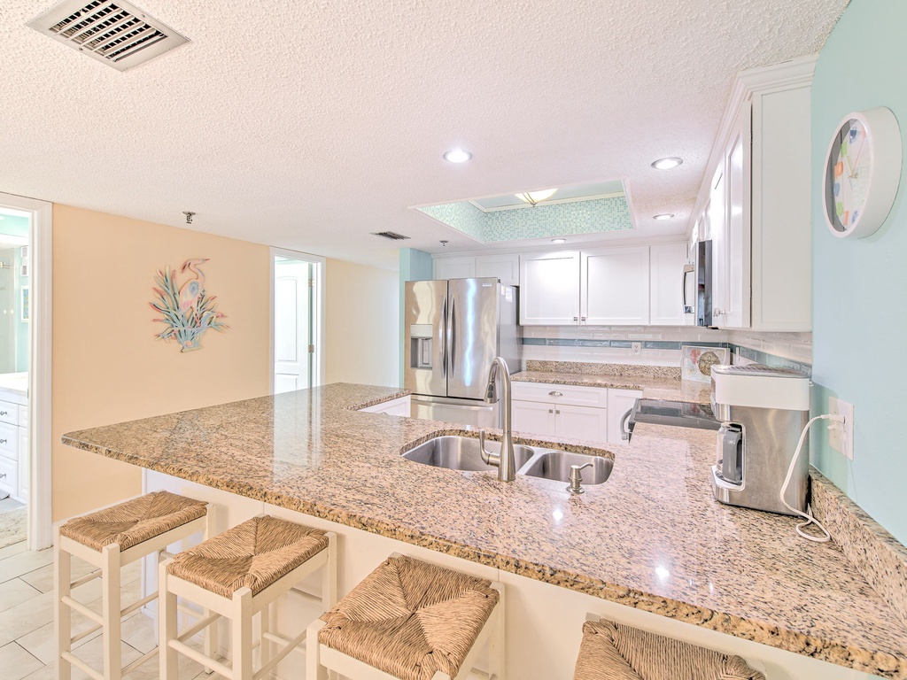 Your open kitchen features granite counters, stainless appliances, and wicker bar stools perfect for morning coffee or casual meals together.