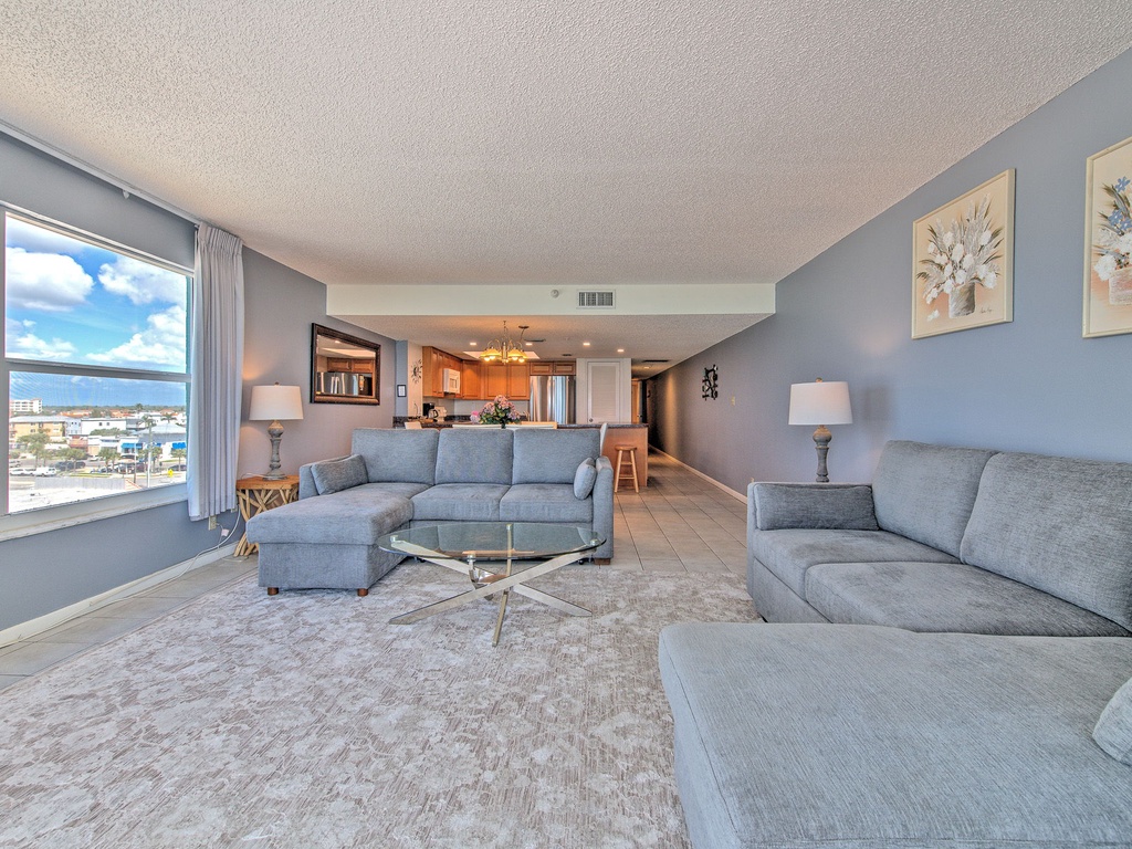 Relax in your spacious living room featuring plush sectional seating and stunning city views through floor-to-ceiling windows.