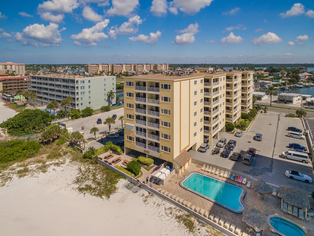 Beachfront condo building with sparkling pool and direct beach access in sunny Florida coastal community.