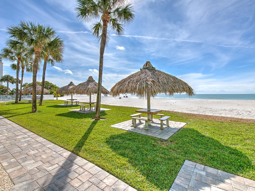 Beautiful beachfront area with thatched umbrella seating and pristine white sand stretching to turquoise waters.