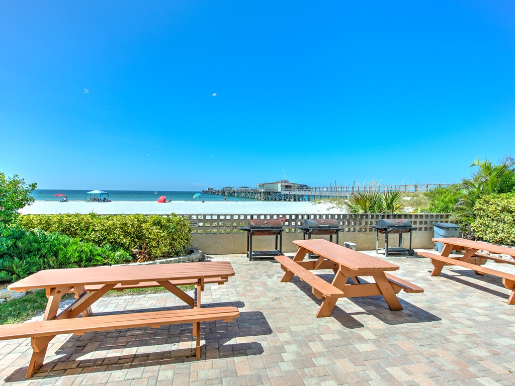 Beachfront dining area with wooden picnic tables overlooking pristine white sand and turquoise waters, perfect for outdoor meals.