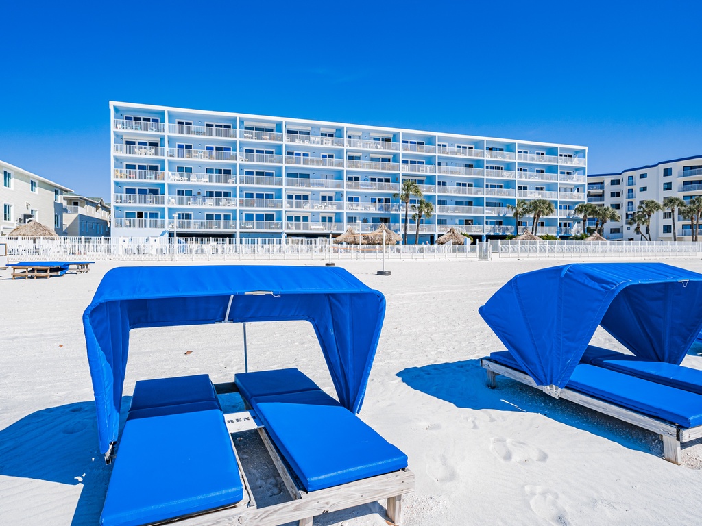 Beachfront resort with private cabanas and comfortable loungers on pristine white sand beneath brilliant blue skies.
