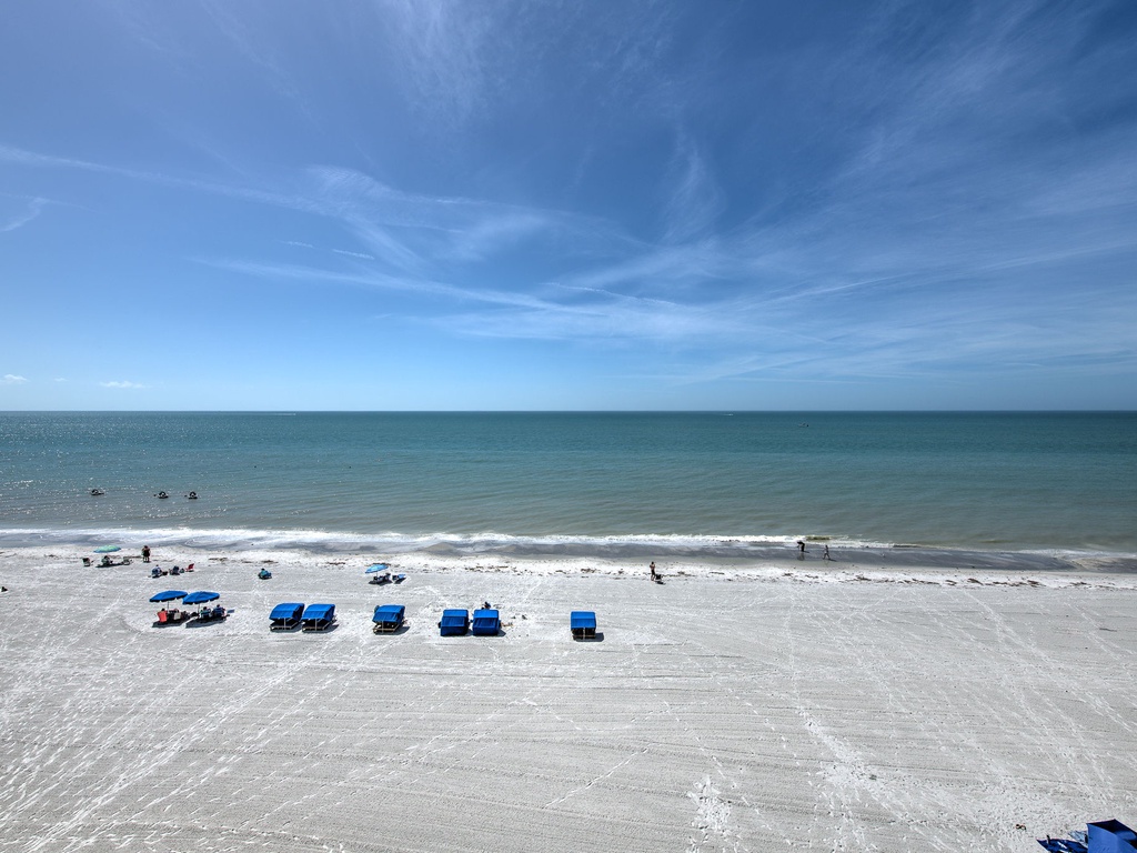 Pristine white sand beach with turquoise waters stretching to the horizon under brilliant blue skies.