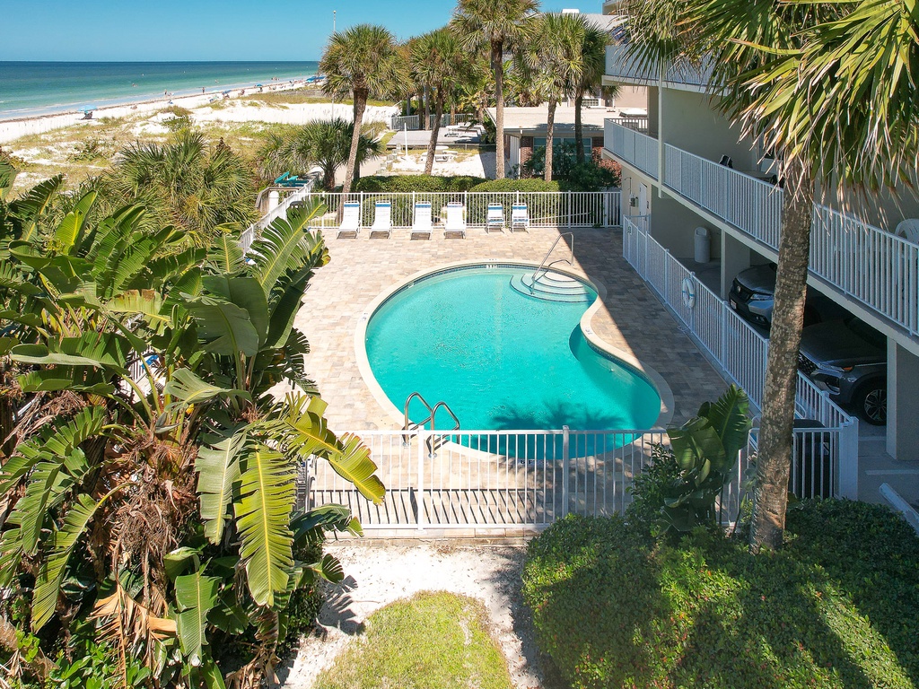 Beachfront property featuring a curved swimming pool surrounded by tropical palms and white sand beaches.