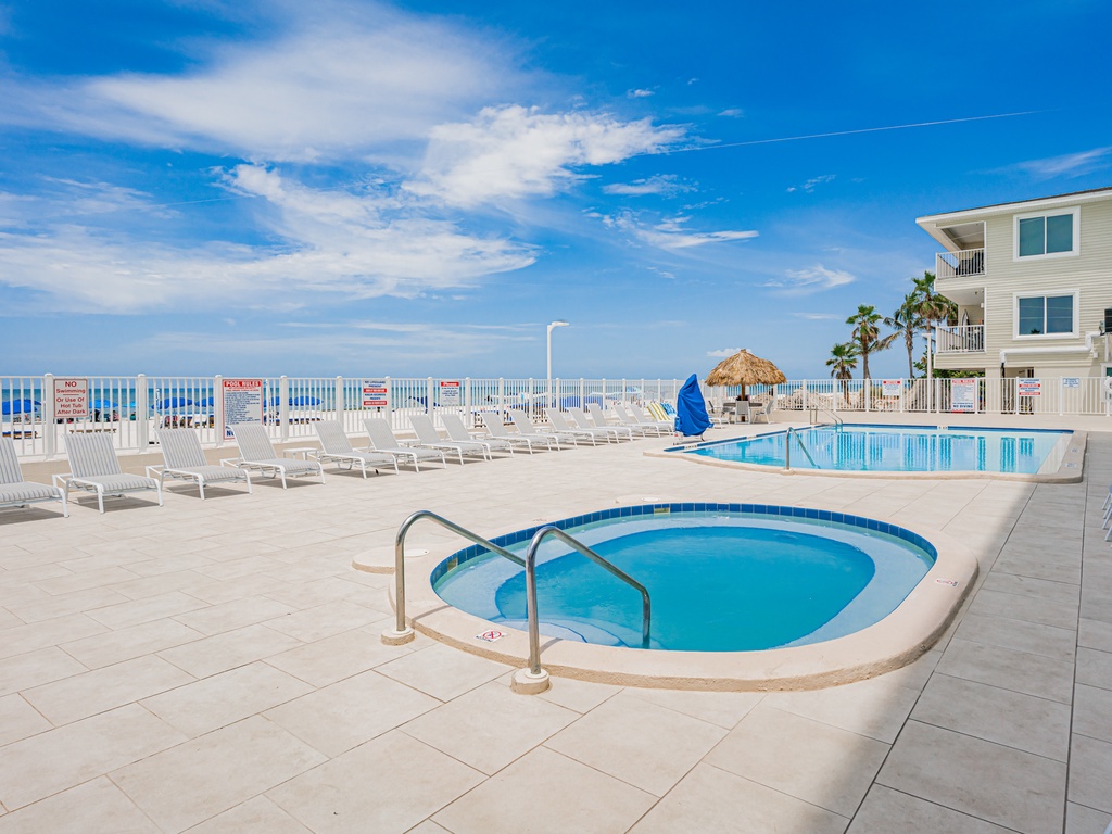Beachfront pool deck with hot tub and white sand beach access beyond the fence.