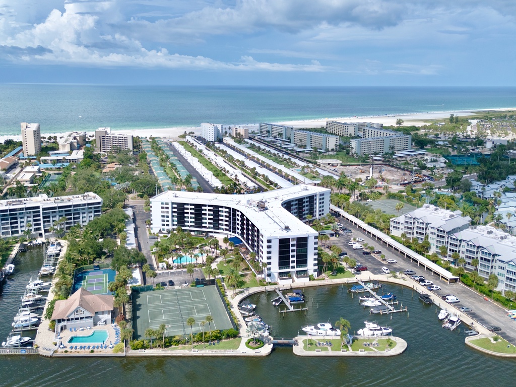 Aerial view of a waterfront resort property with expansive grounds, nestled between tranquil waters and lush tropical landscaping.