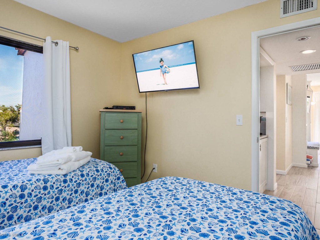 Your peaceful bedroom features twin beds with ocean-inspired linens, wall-mounted TV, and storage for your vacation essentials.