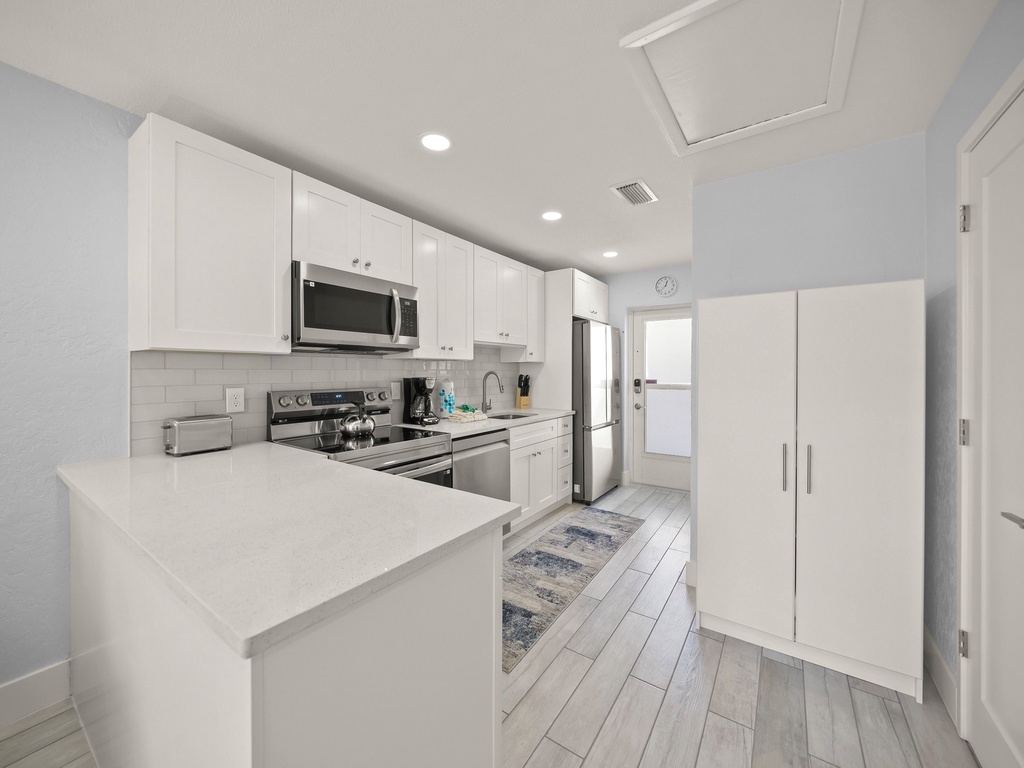Your pristine kitchen awaits with gleaming white cabinets, stainless appliances, and a spacious island perfect for morning coffee or meal prep.
