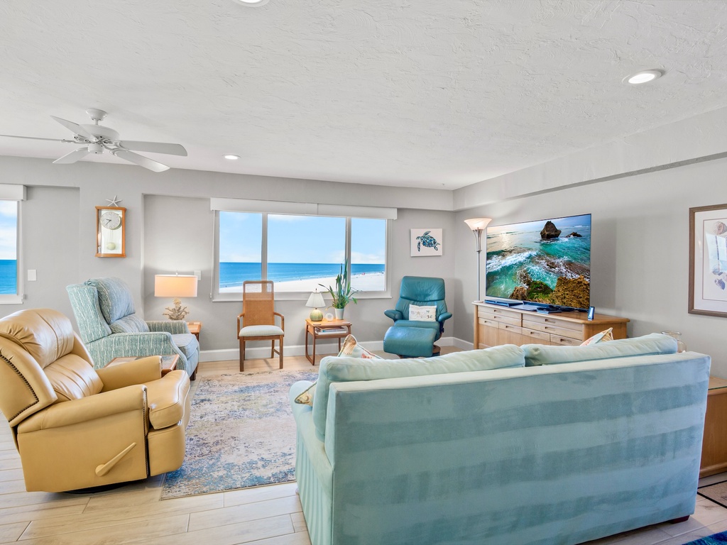 Sink into plush seating while ocean waves fill your view through floor-to-ceiling windows in this bright, coastal-themed living space.