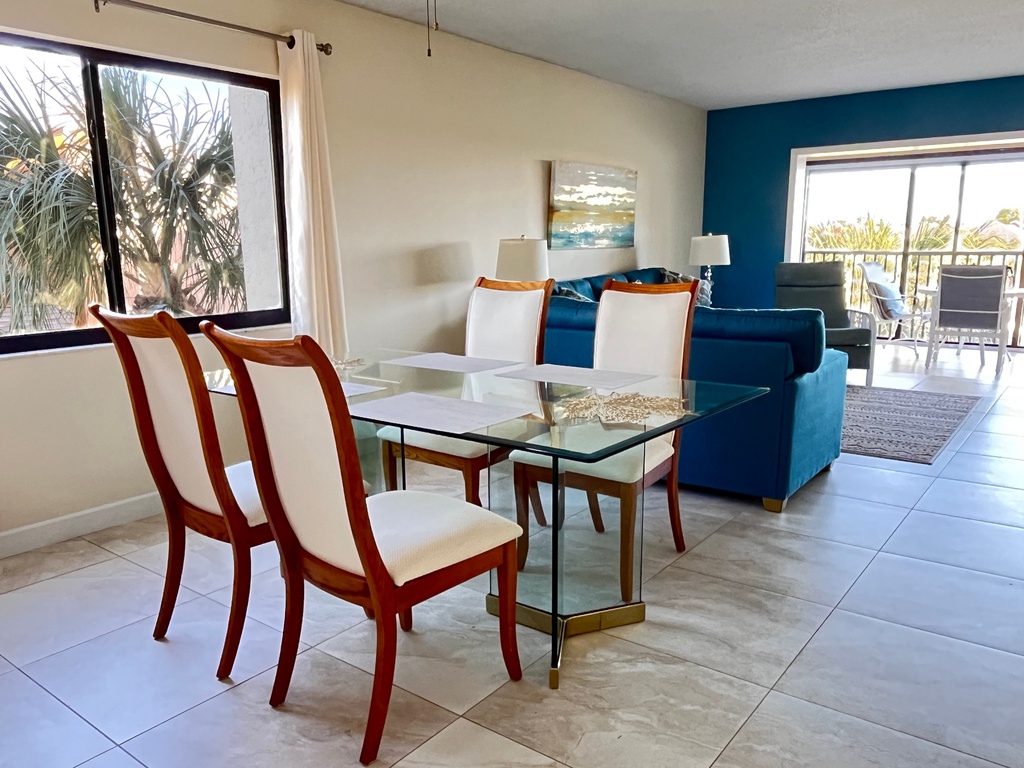 Unwind in your bright, coastal living space with modern glass dining and plush navy seating overlooking tropical palms.