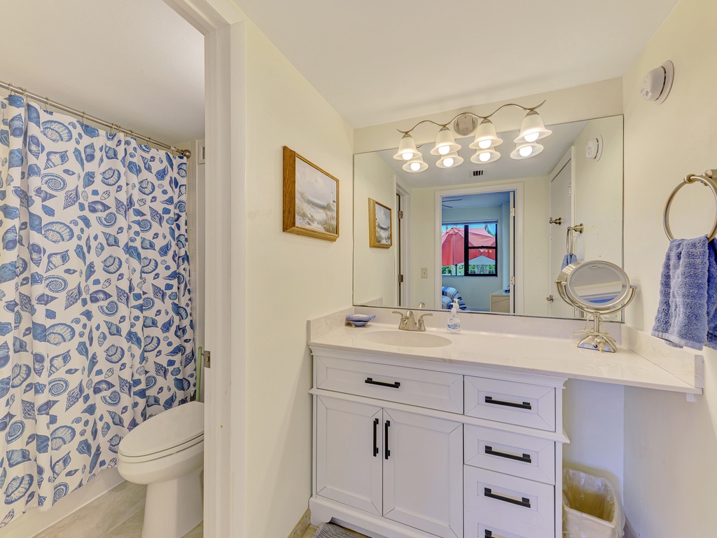 Your private bathroom features coastal charm with seashell shower curtain, crisp white vanity, and Hollywood-style lighting for perfect morning routines.