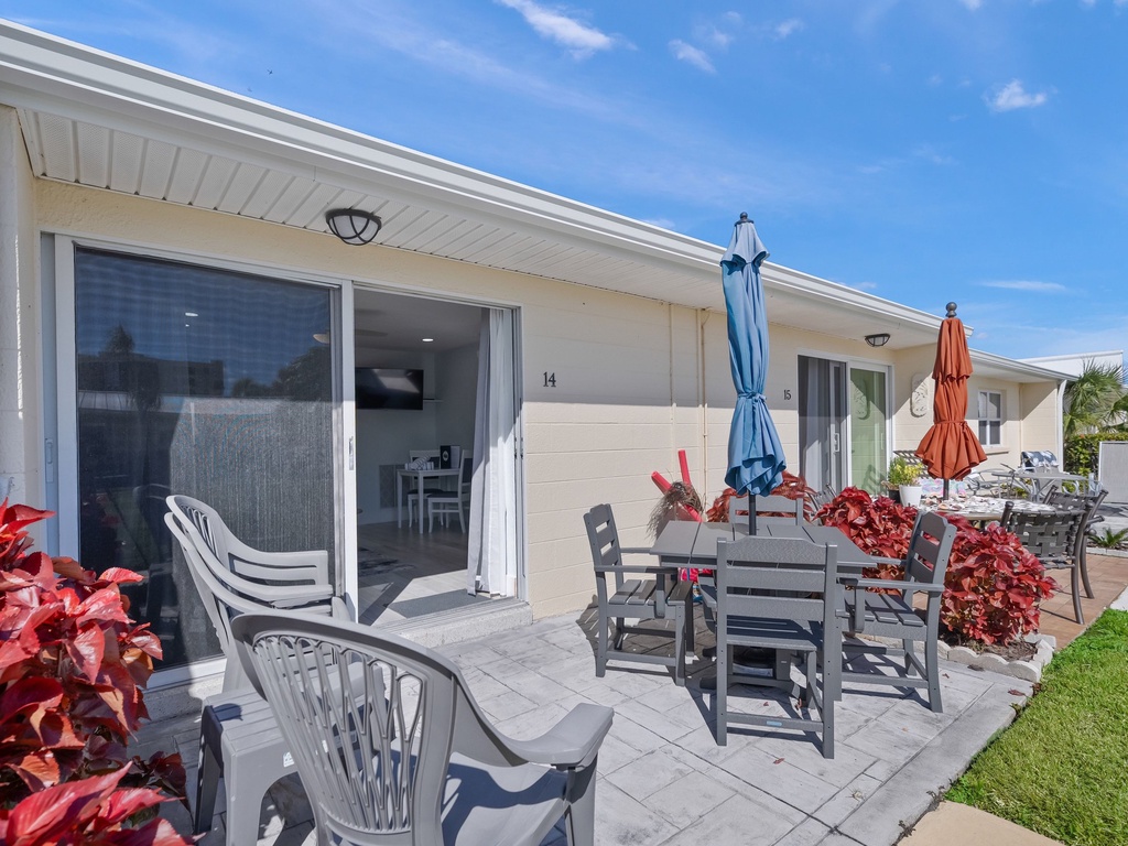 Step onto your private patio where vibrant tropical plants frame outdoor dining under bright blue skies.
