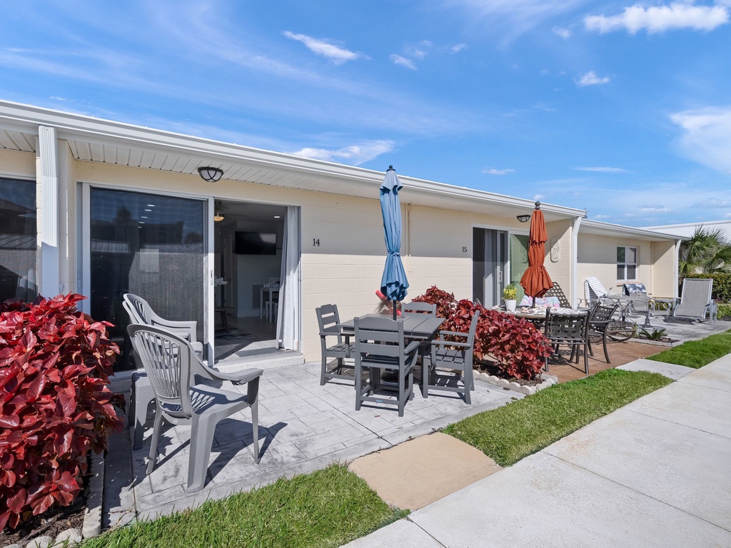 Stylish modern property featuring individual units with private patios, outdoor dining areas, and vibrant landscaping under sunny skies.