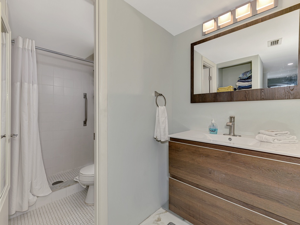 Step into your pristine bathroom featuring modern wood vanity, spacious shower, and fresh towels waiting for your arrival.
