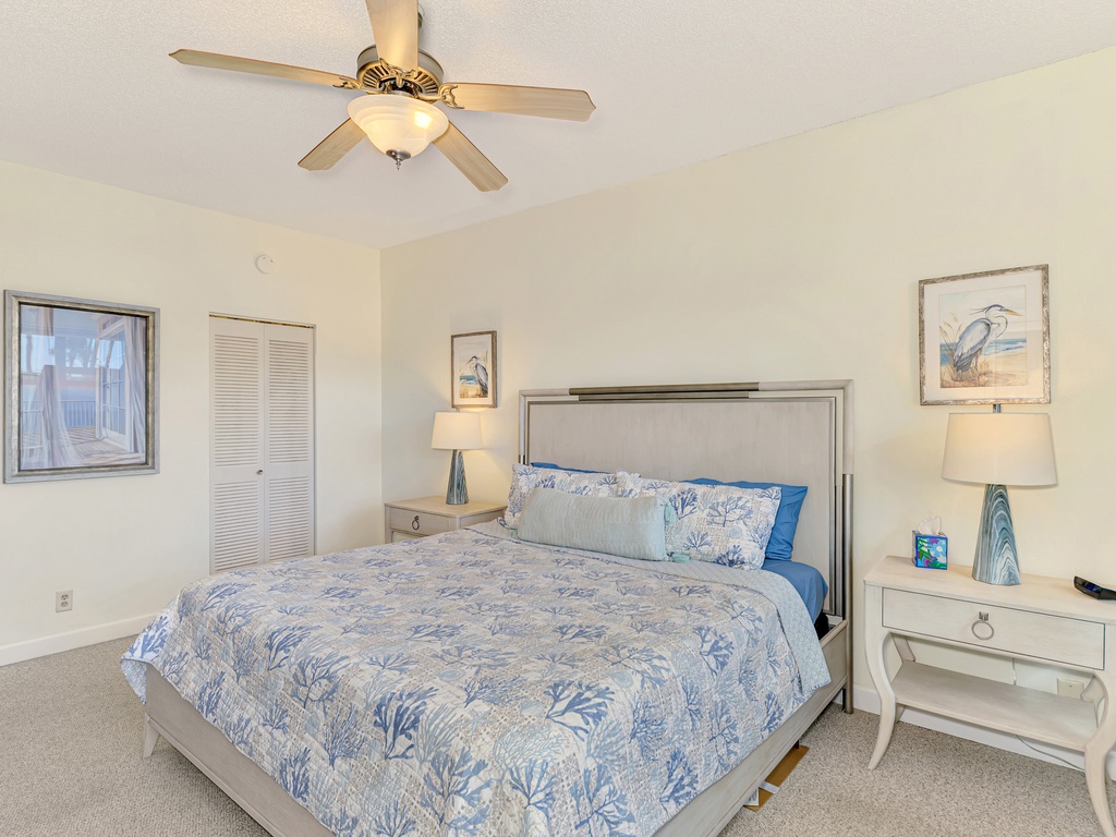 Drift off in your peaceful bedroom with coastal blue bedding, gentle ceiling fan, and nautical artwork creating the perfect seaside retreat.