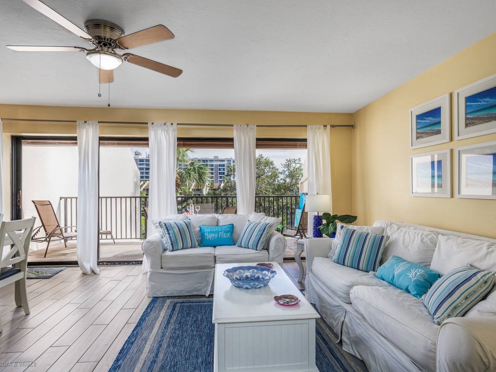 Relax in your bright living room with coastal decor, ceiling fan, and balcony access to enjoy comfortable indoor-outdoor living.