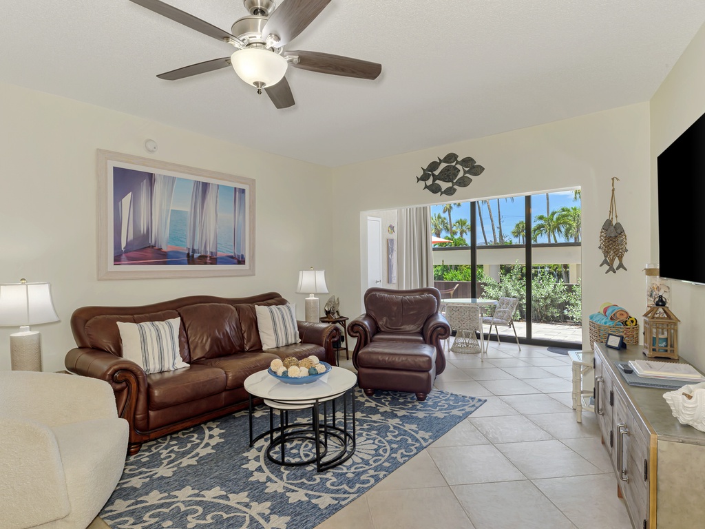 Relax in your inviting living room with plush leather seating, ceiling fan, and tropical views through your private patio doors.