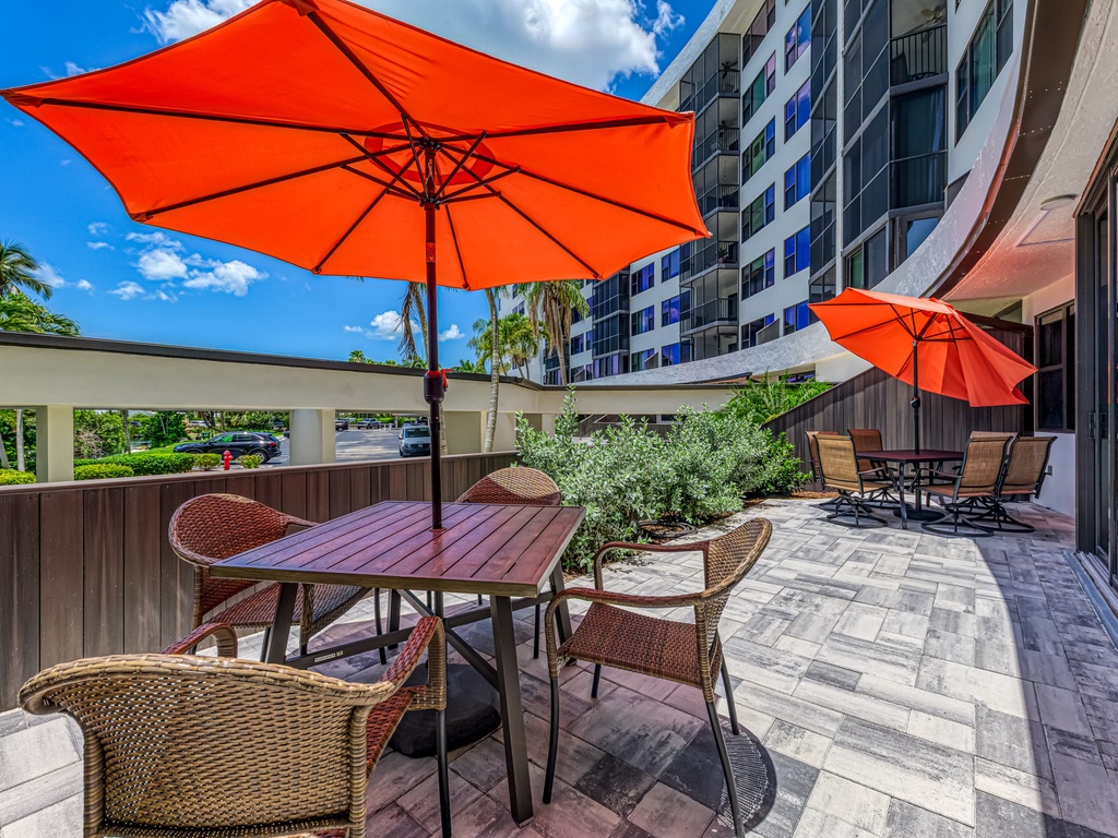Relax at your private outdoor dining table under bright orange umbrellas, surrounded by modern amenities and tropical landscaping.
