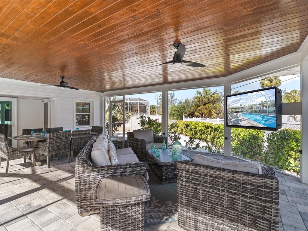 Relax in your elegant screened patio with stunning wood ceiling and pool views, featuring comfy wicker seating and entertainment center.
