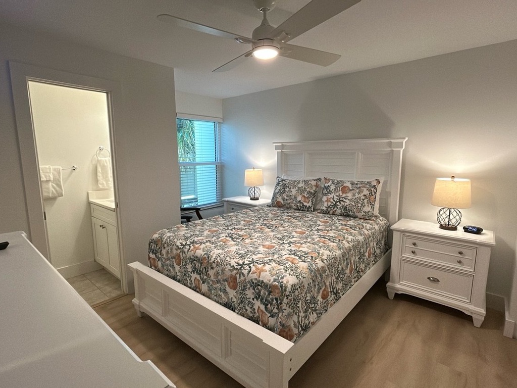 Your peaceful bedroom features a comfortable queen bed with botanical bedding, soft lighting from matching nightstand lamps, and a ceiling fan for your perfect sleep temperature.