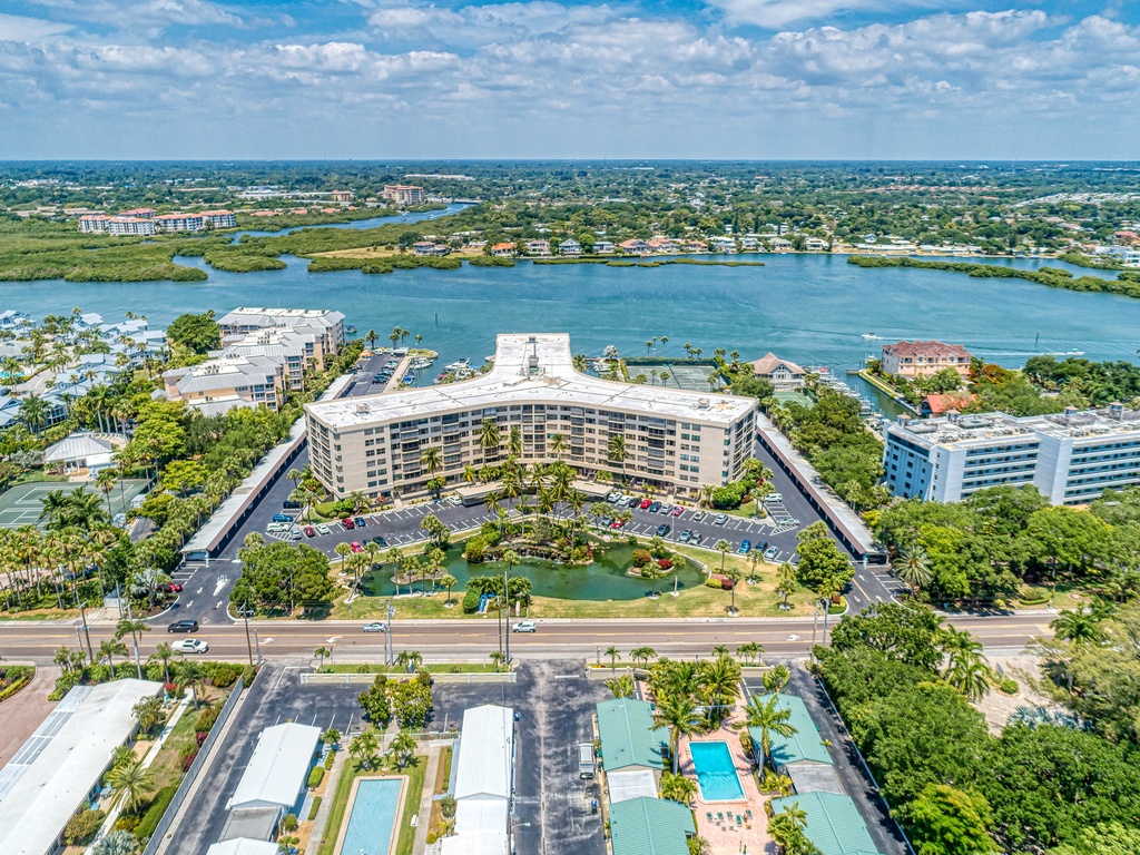 Aerial view of a waterfront resort property with expansive grounds, nestled between tranquil waters and lush tropical landscaping.