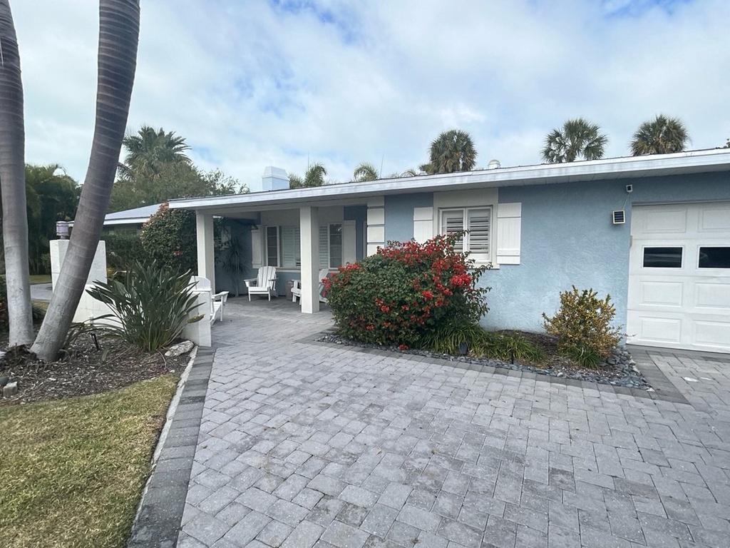 Charming coastal retreat with elegant brick driveway, tropical landscaping, and convenient parking. Palm trees frame this inviting blue home.