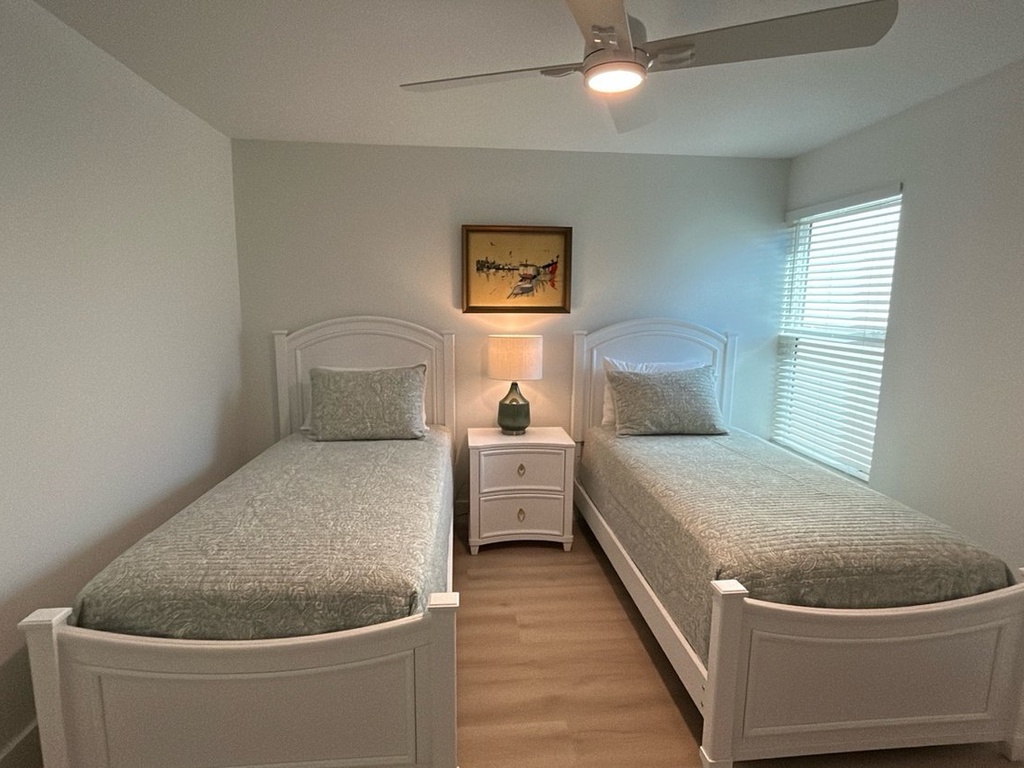 Rest peacefully in your twin bedroom with matching white beds, soft gray linens, and gentle ceiling fan breeze.