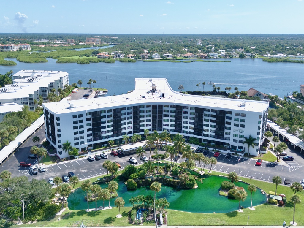 Tropical resort building with waterfront setting, featuring lush palm trees and landscaped grounds under bright blue skies.
