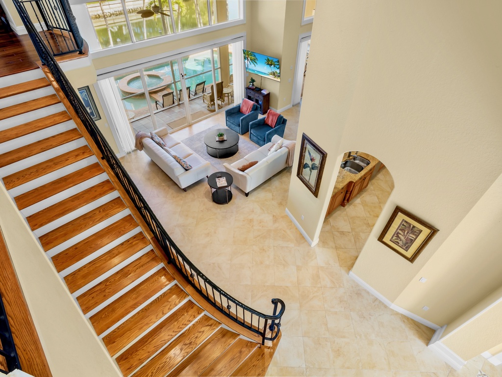 Descend the elegant curved staircase into your spacious living area, where modern comfort meets luxury with soaring ceilings and pool views.
