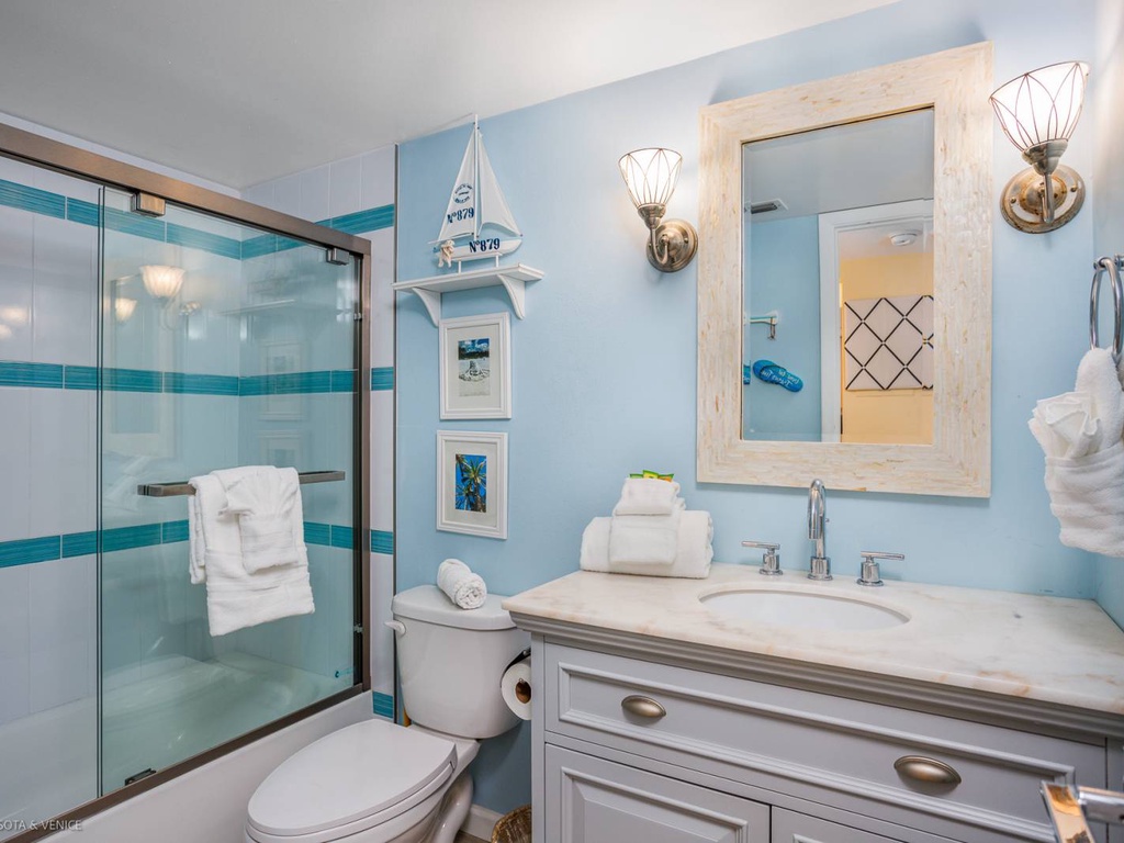 Refresh in your coastal-themed bathroom with glass shower, marble vanity, and charming nautical touches that create a serene seaside escape.