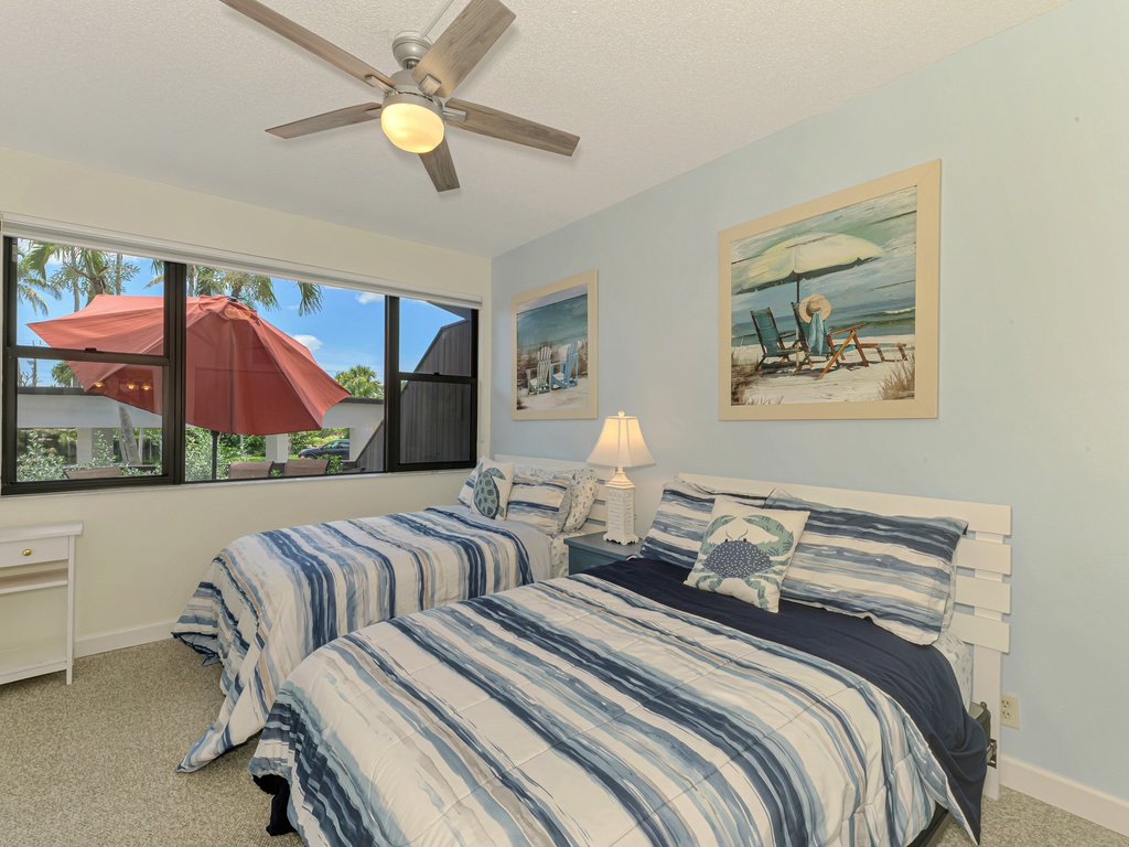 Your coastal bedroom features twin beds with beach-themed decor, a ceiling fan for comfort, and cheerful views of the tropical outdoors.