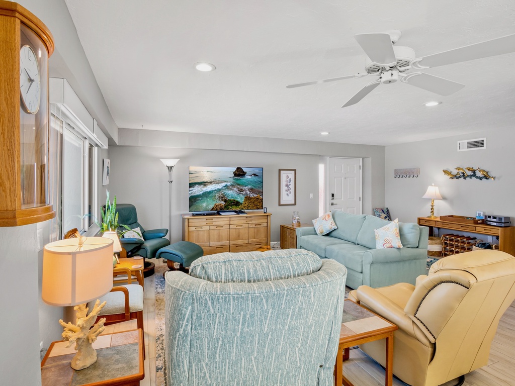 Relax in your spacious living room with coastal decor, ceiling fan, and comfortable seating perfect for unwinding after beach days.