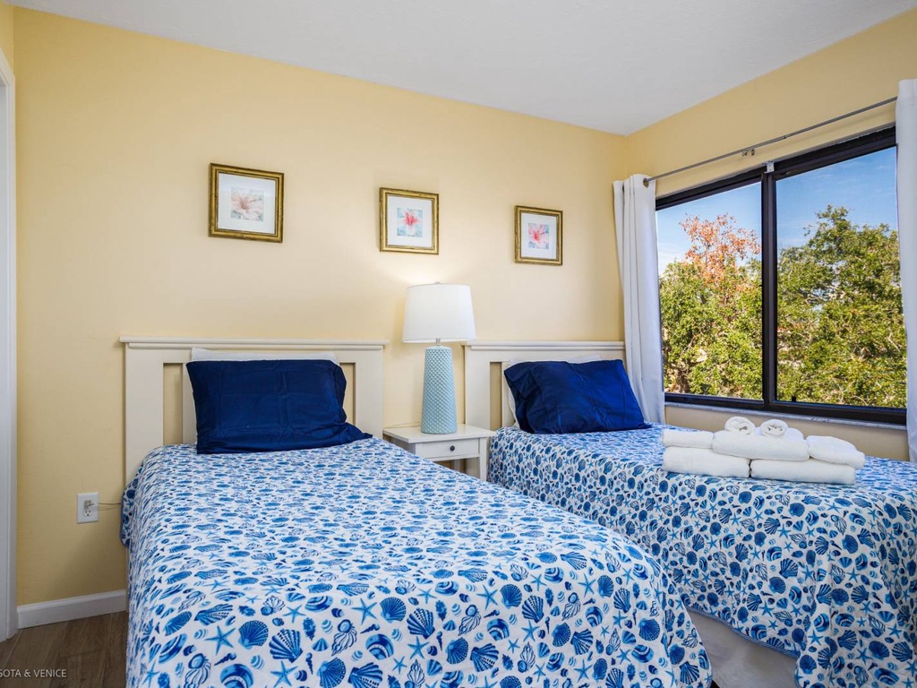 Unwind in your bright twin bedroom with cheerful blue bedding and peaceful garden views streaming through large windows.