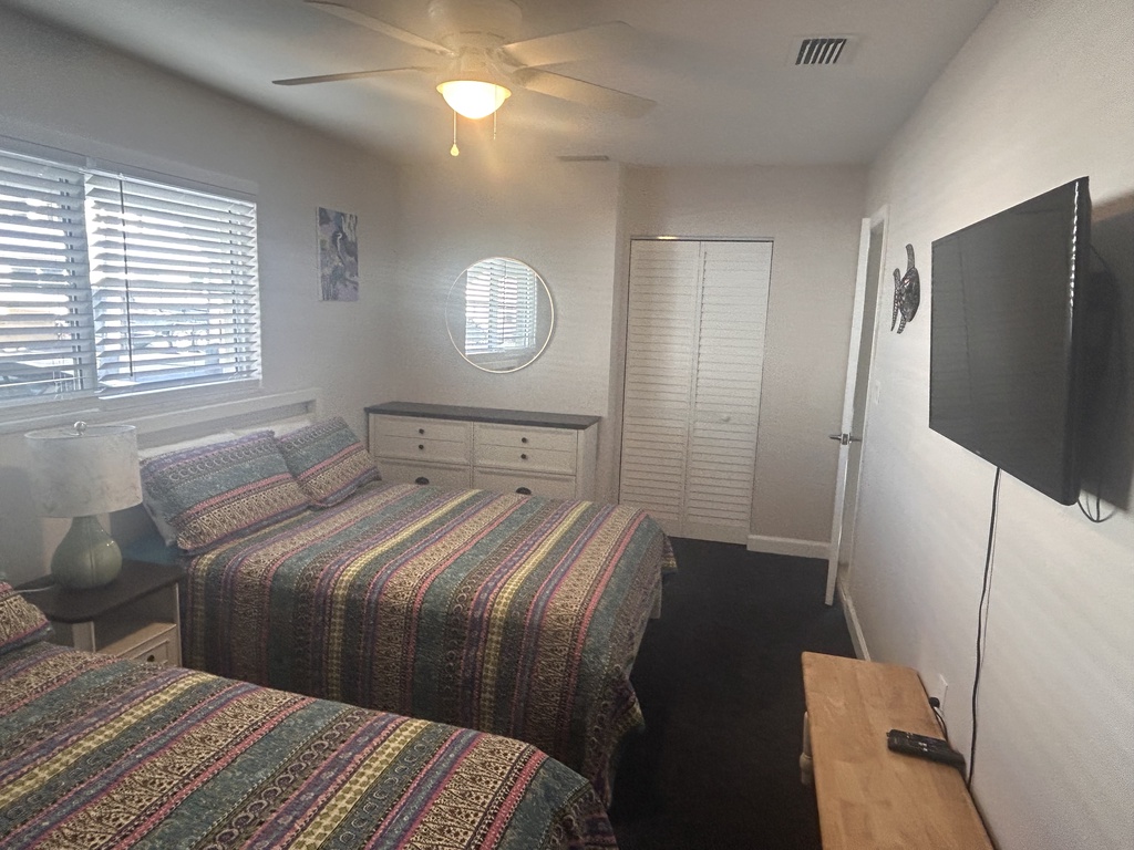 Your comfortable bedroom features two cozy beds with colorful quilts, a ceiling fan for gentle breezes, and entertainment at your fingertips.