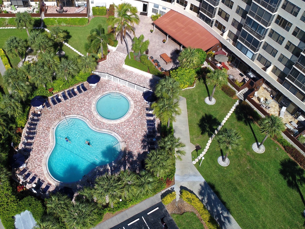 Aerial view showcasing the resort-style pool area with tropical landscaping, surrounded by modern apartment buildings and lush green spaces.