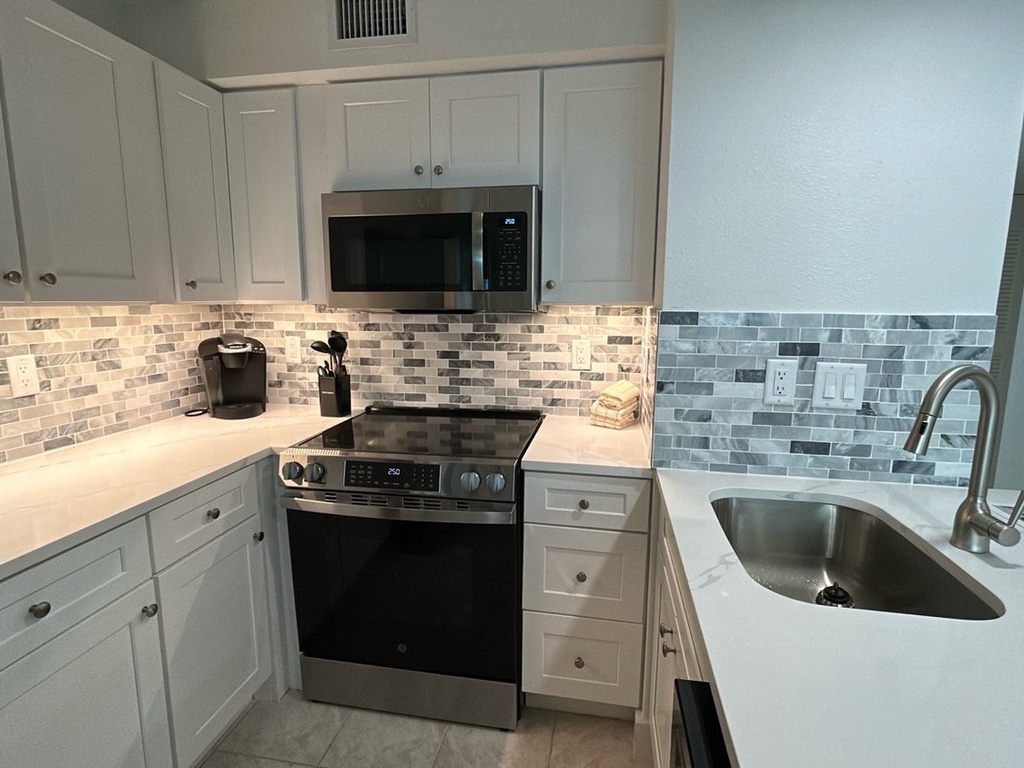 Cook your favorite meals in this sleek, fully-equipped kitchen featuring white cabinets, modern appliances, and elegant tile backsplash.