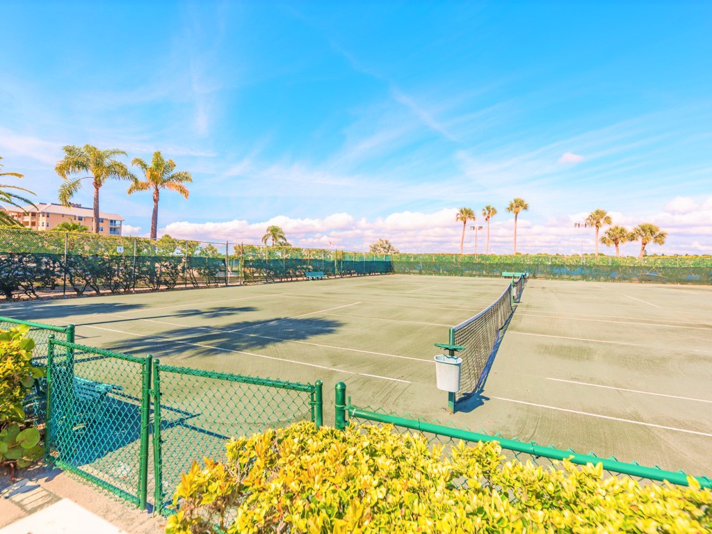 Tennis court surrounded by tropical palms and lush landscaping under beautiful blue skies.