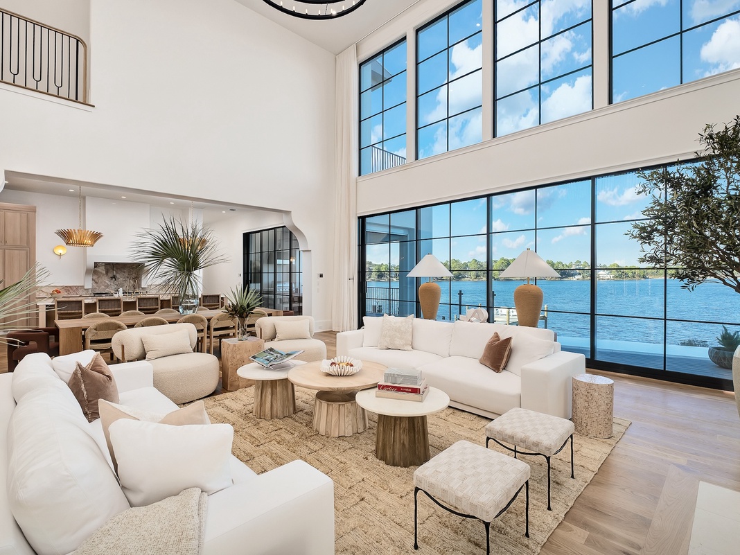Unwind in this stunning waterfront living room where floor-to-ceiling windows frame breathtaking lake views, plush white sofas invite relaxation, and natural light fills the space.