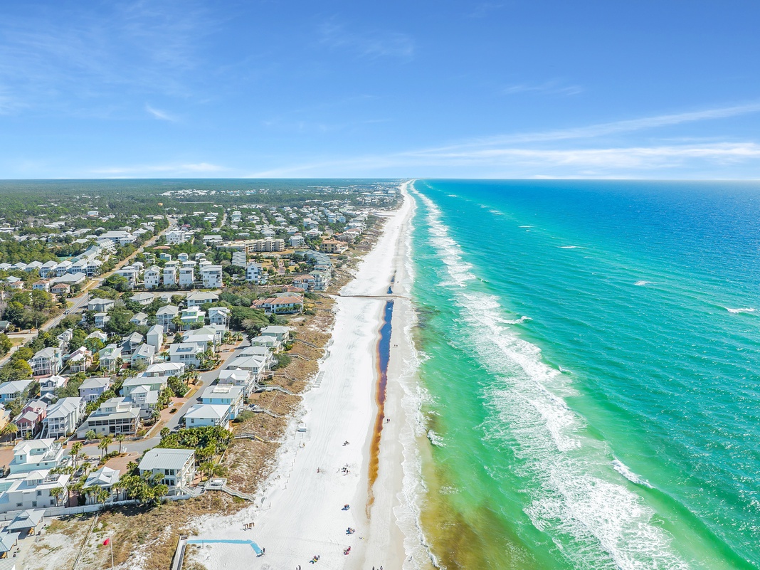 Stunning aerial view of pristine white sand beaches meeting crystal-clear turquoise waters, with beachfront vacation properties dotting the coastline.