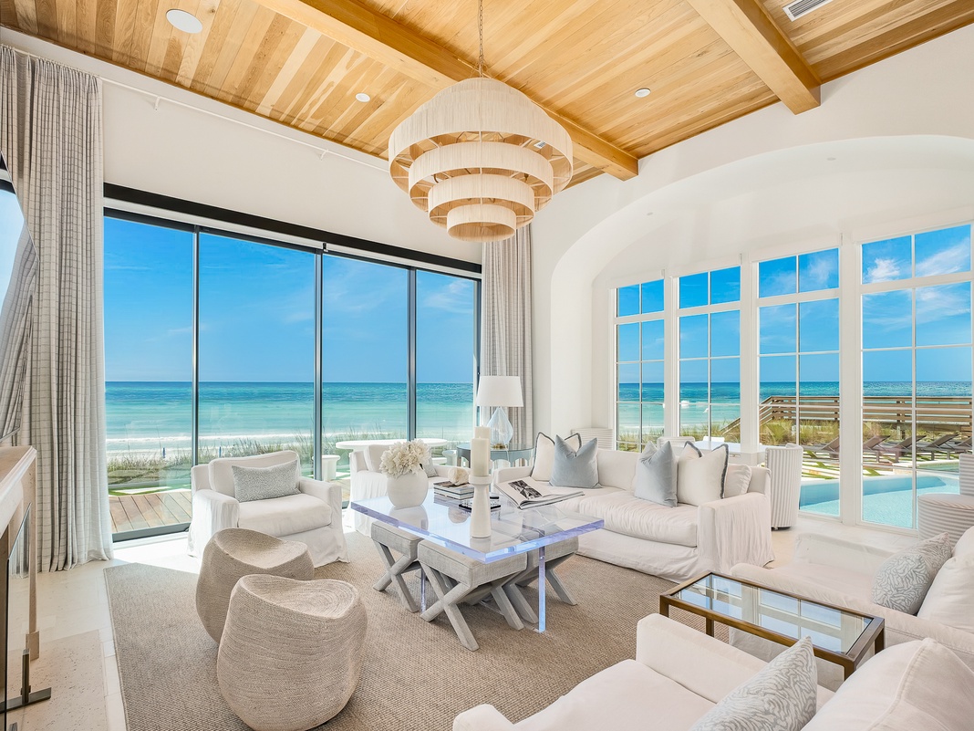 Sink into plush white sofas while gazing at endless ocean views through floor-to-ceiling windows in your elegant beachfront retreat.