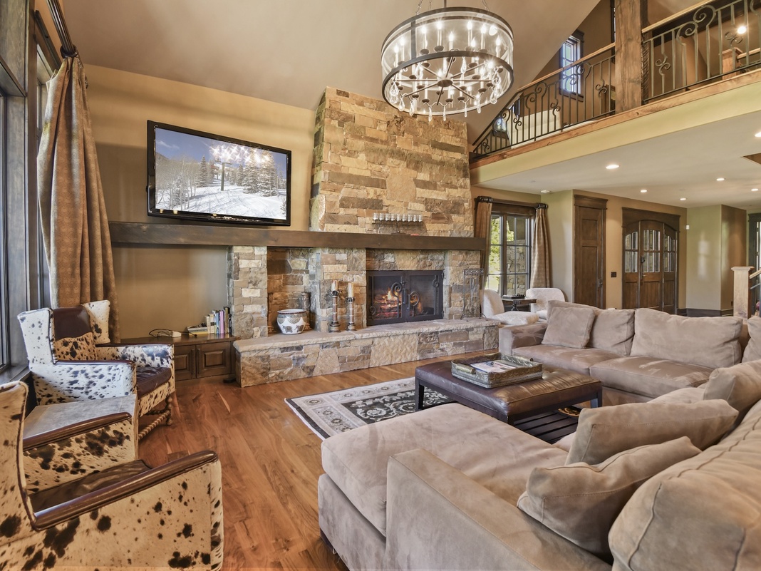Sink into plush seating by the stone fireplace, where your evenings unfold with warmth, elegance, and mountain charm beneath a stunning chandelier.