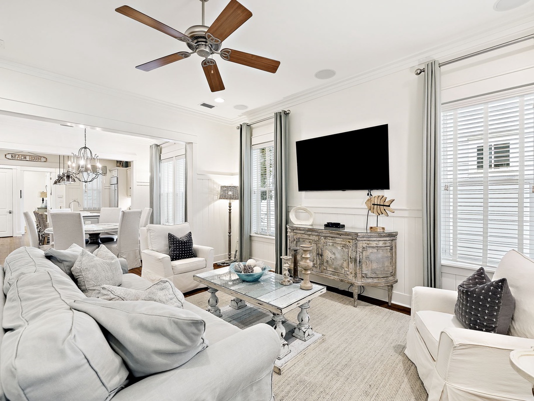 Sink into plush sofas in your elegant living room, where coastal charm meets modern comfort beneath a gentle ceiling fan breeze.