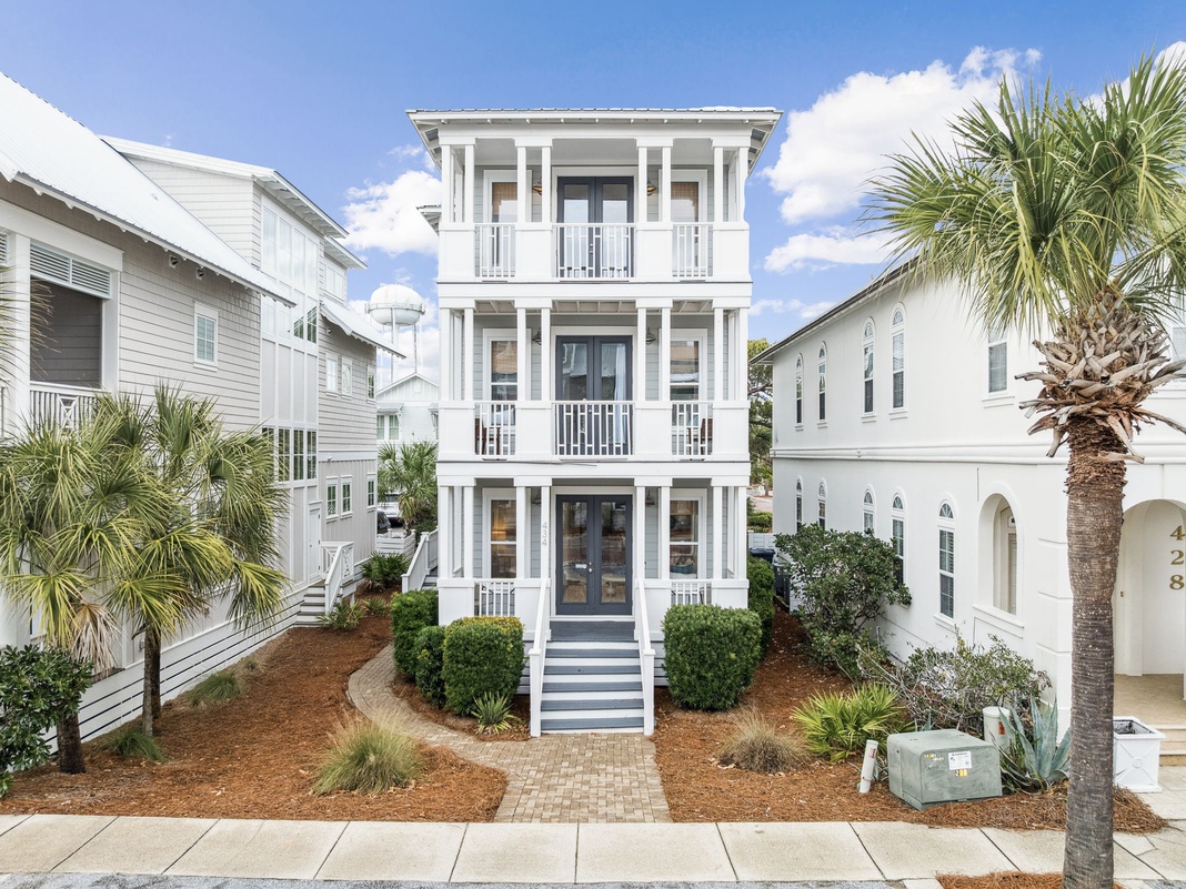 A charming three-story coastal home with white railings and palm trees in a peaceful neighborhood setting.
